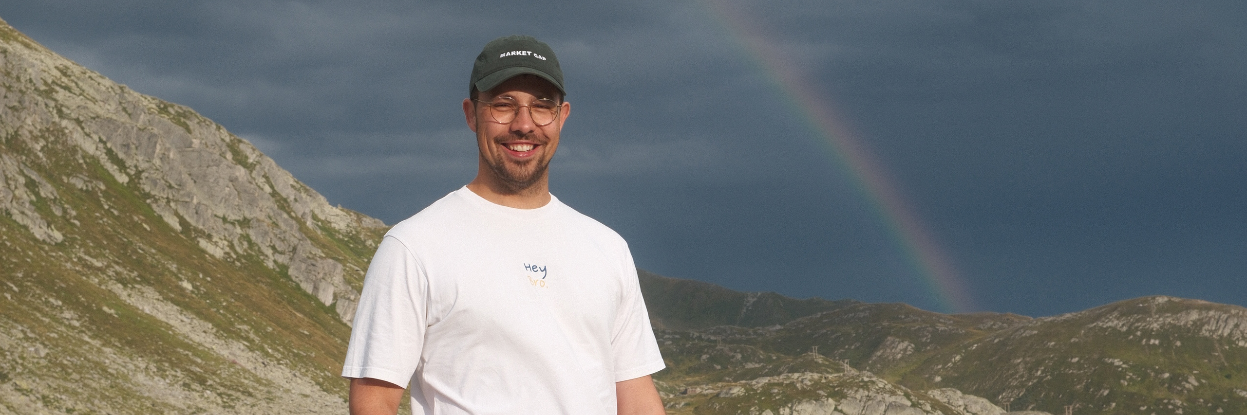 Dario Glasl in den Bergen, im Hintergrund ein Regenbogen